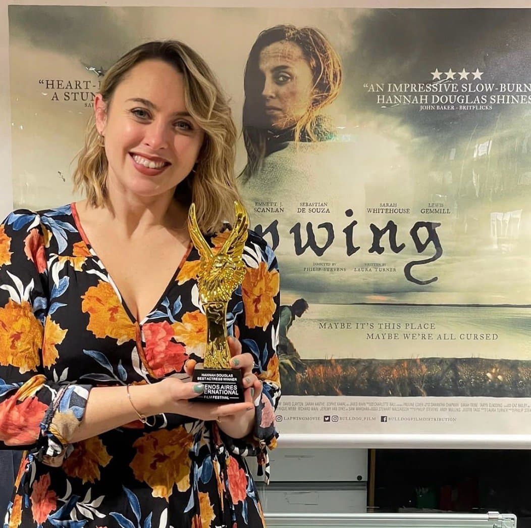 Hannah holding her Best Actress award from the Buenos Aires International Film Festival, in front of the poster for the film Lapwing