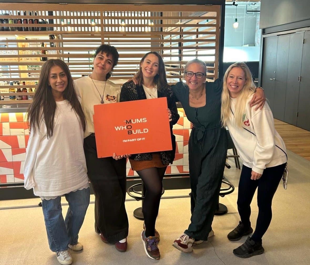 Five women smiling together after a LoudHer community event, one holding a Mums Who Build sign