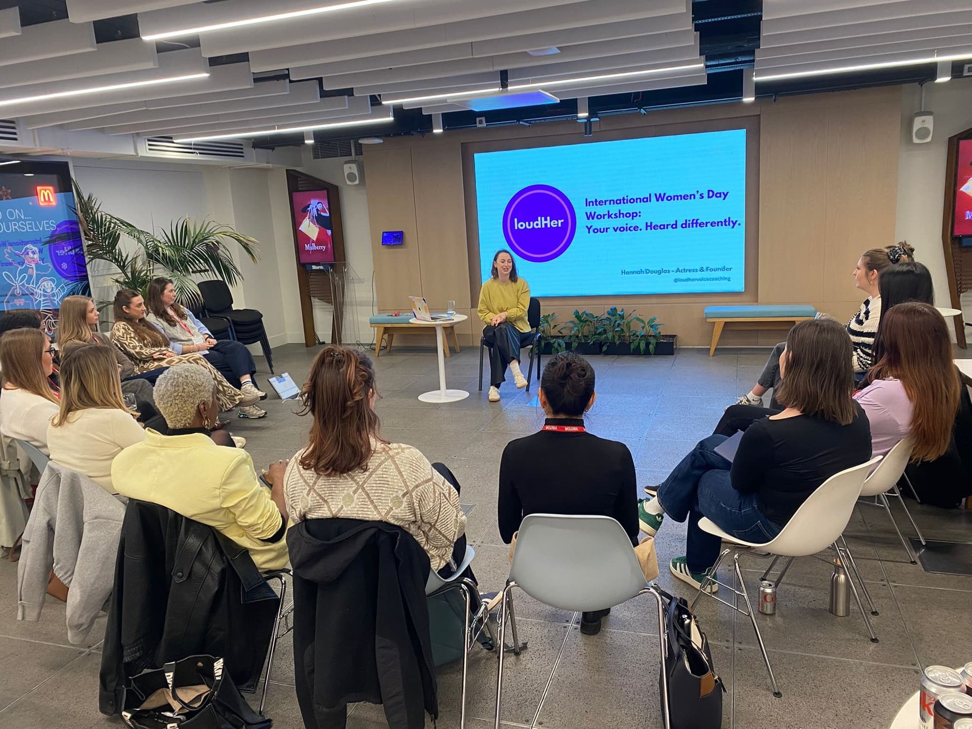 Hannah leading an International Women's Day workshop, seated at the front with a circle of attendees around her